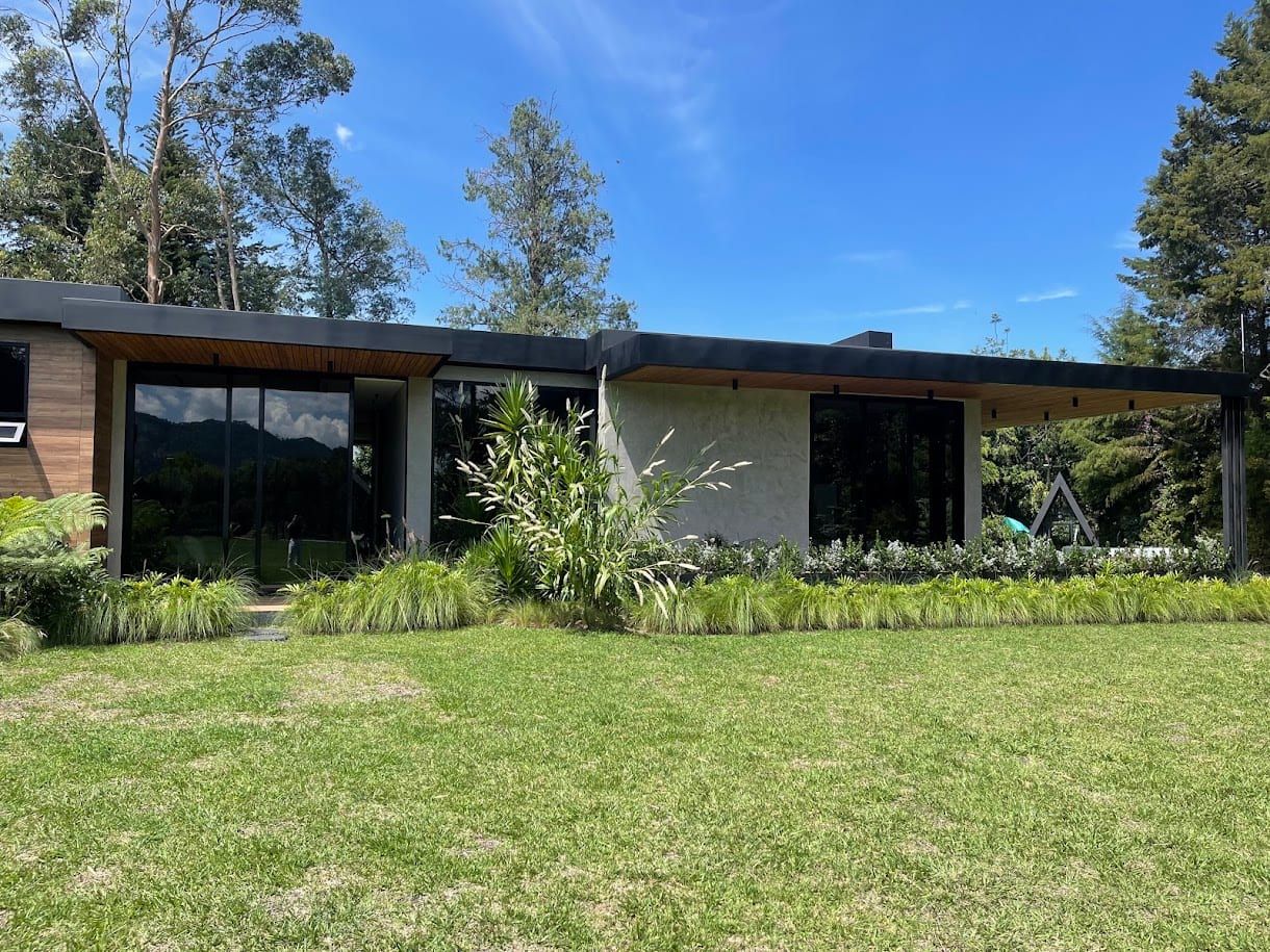 Fachada de la casa en madera y planos negros, rodeada de jardín