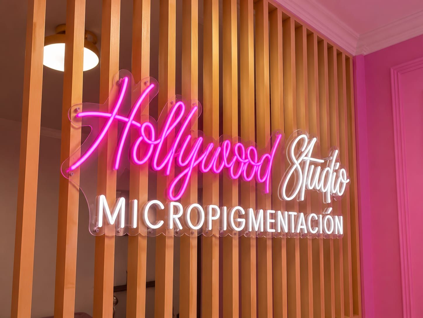 Aviso de neón "Hollywood Studio Micropigmentación" sobre listones de madera