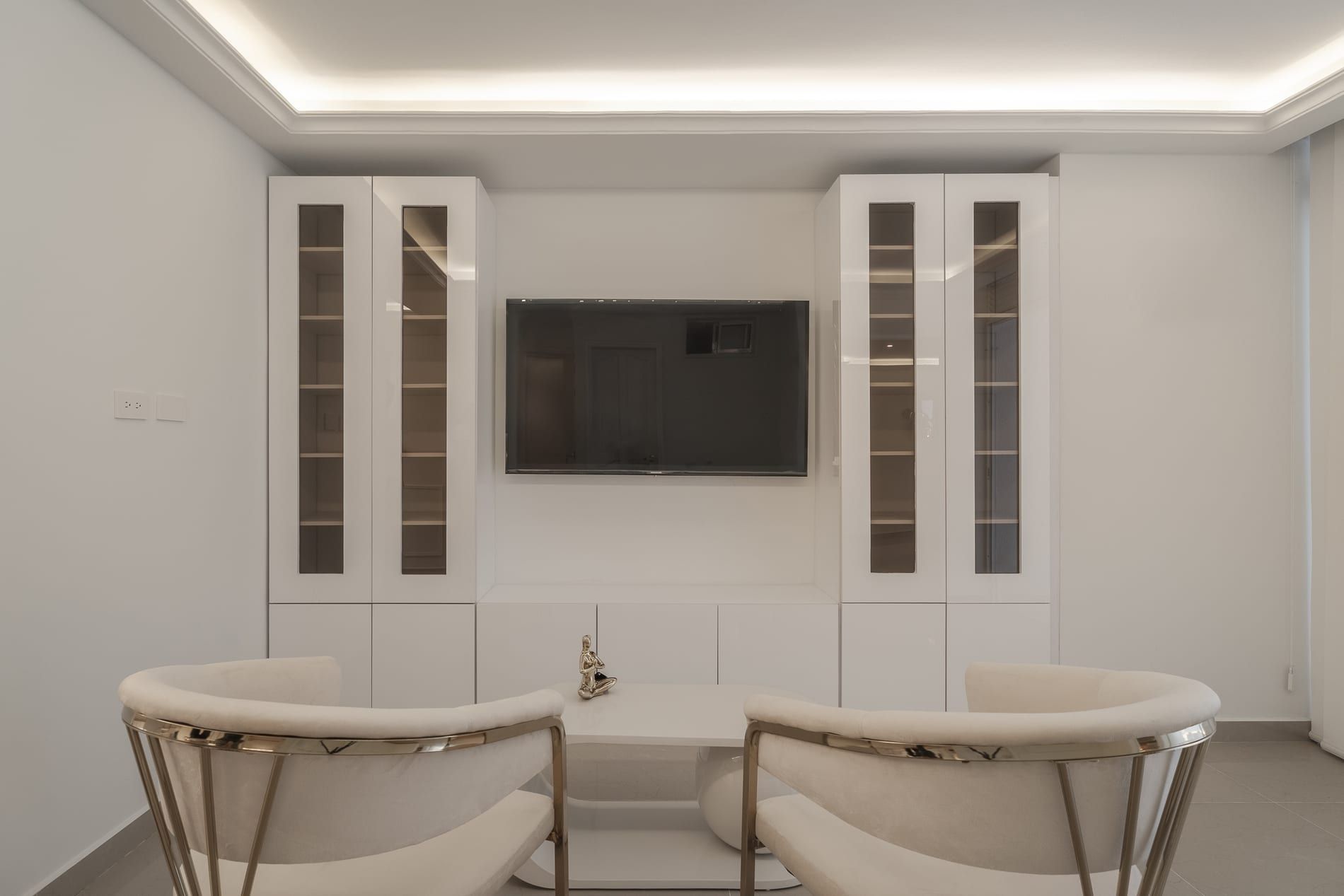 Mueble de televisor con vitrinas blancas y sillas con acentos dorados