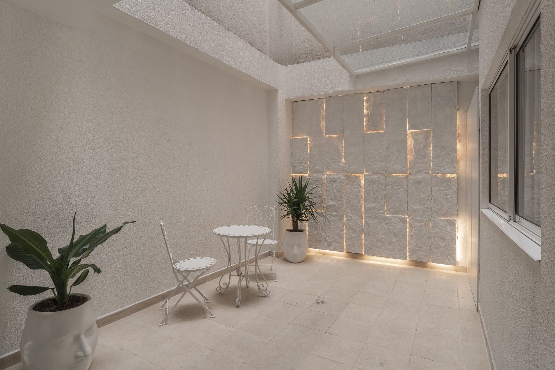 Patio interior con muro de piedra retroiluminado, mesa y planta