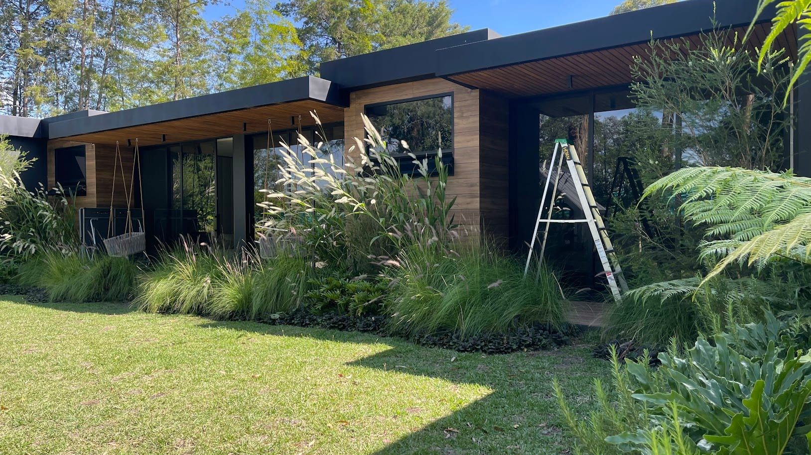Costado de la casa con revestimiento de madera y plantas junto a un camino de losas