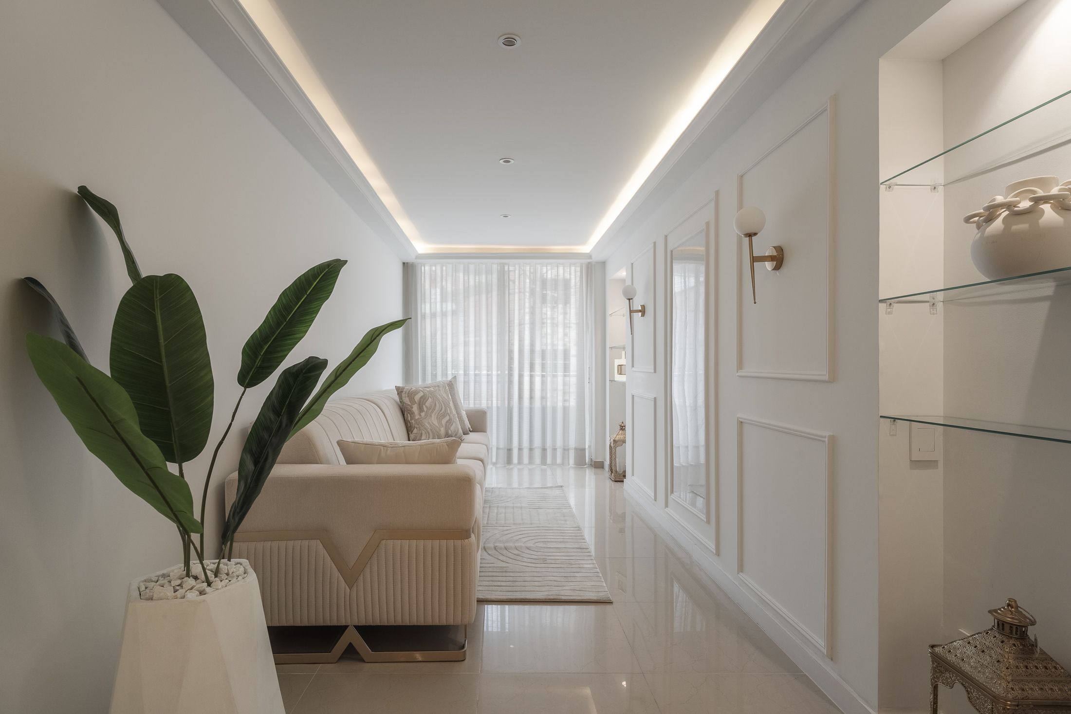 Sala en tonos blancos con iluminación indirecta, sofá crema y boiserie